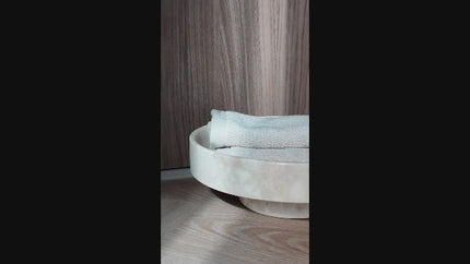 Ronde schaal op voet gemaakt van beige natuursteen Aquanova Blake in kleur Desert met luxe handdoeken in licht beige Aquanova Athena in kleur Desert